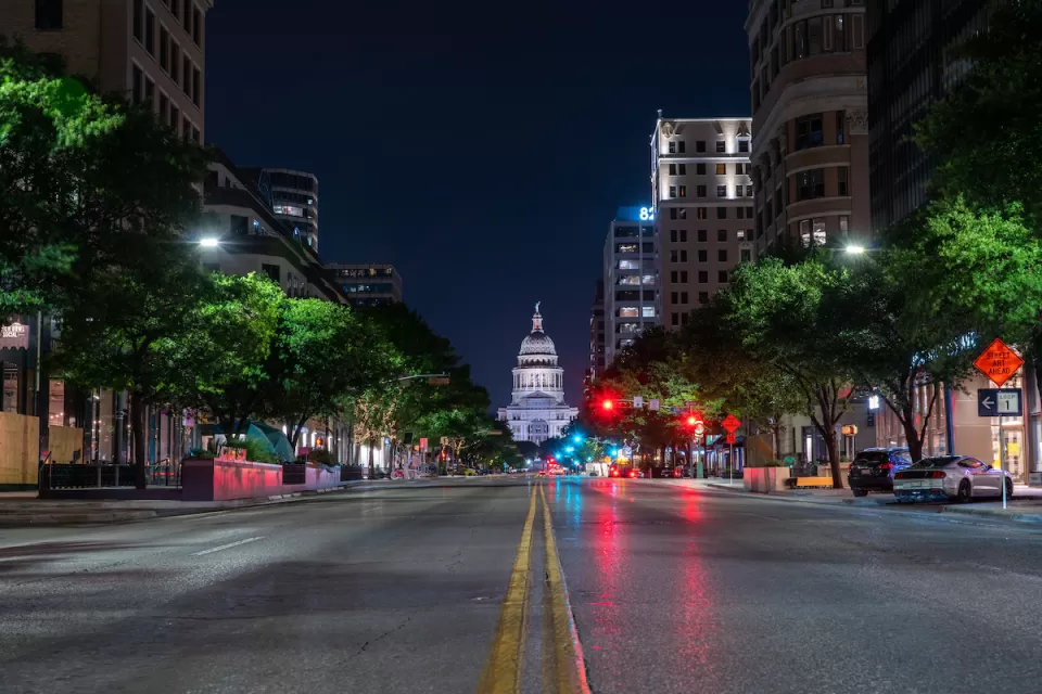Low angle view of Texas state capitol at night from middle of wide street.